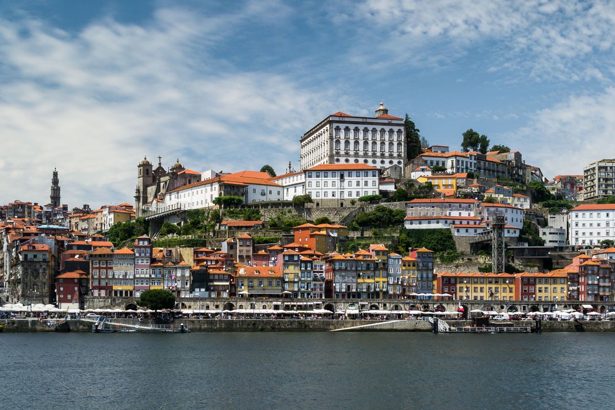 Pohled na historické centrum města Porto s&nbsp;barevnými domy a&nbsp;výraznou budovou kláštera Serra do Pilar na kopci, obklopené řekou Douro.