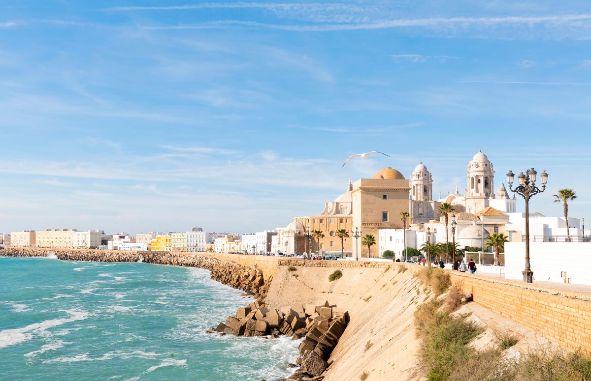 Panorama města Cádiz s pohledem na historické budovy u pobřeží moře a katedrálu v pozadí.