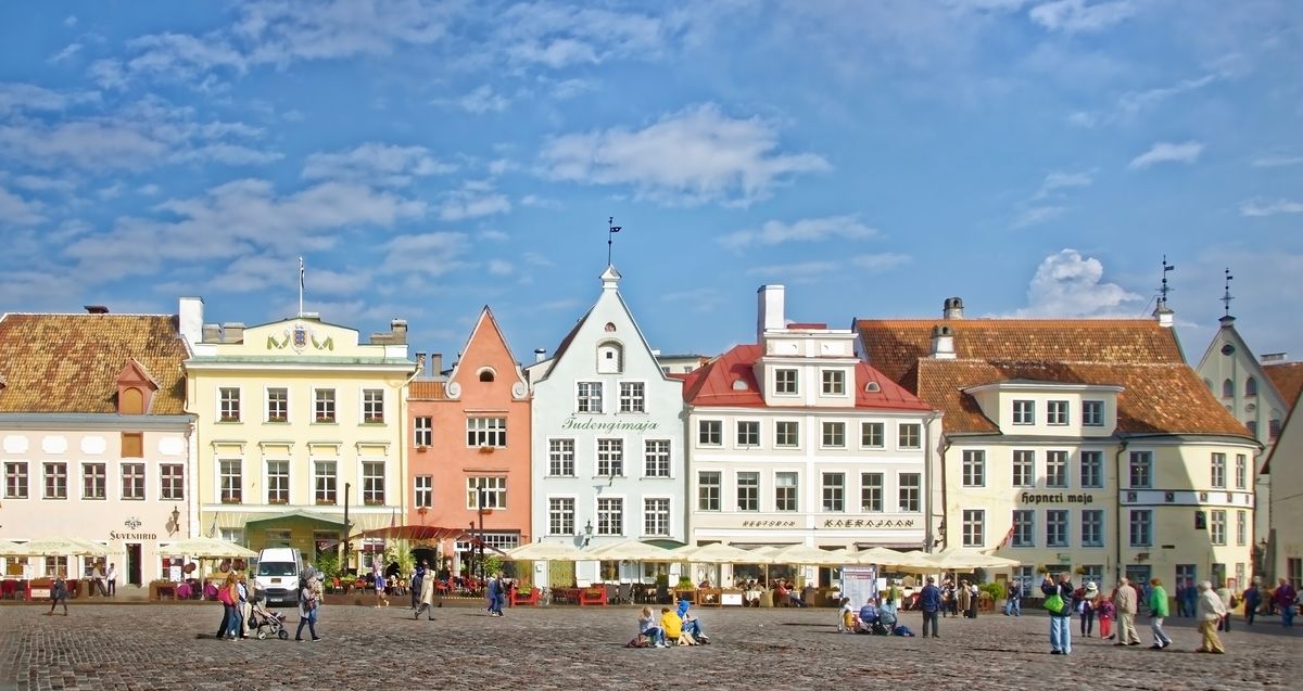 Historické budovy na náměstí v&nbsp;Tallinnu zdobené pestrobarevnými fasádami pod modrou oblohou.