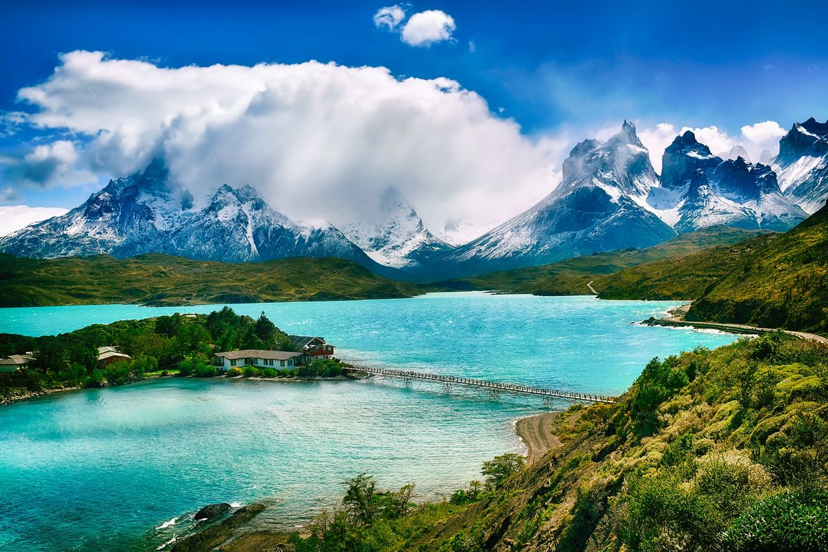 Jezero Pehoé v&nbsp;národním parku Torres del Paine s&nbsp;výraznými horami pokrytými sněhem v&nbsp;pozadí a&nbsp;dřevěným mostem vedoucím k&nbsp;malému poloostrovu.