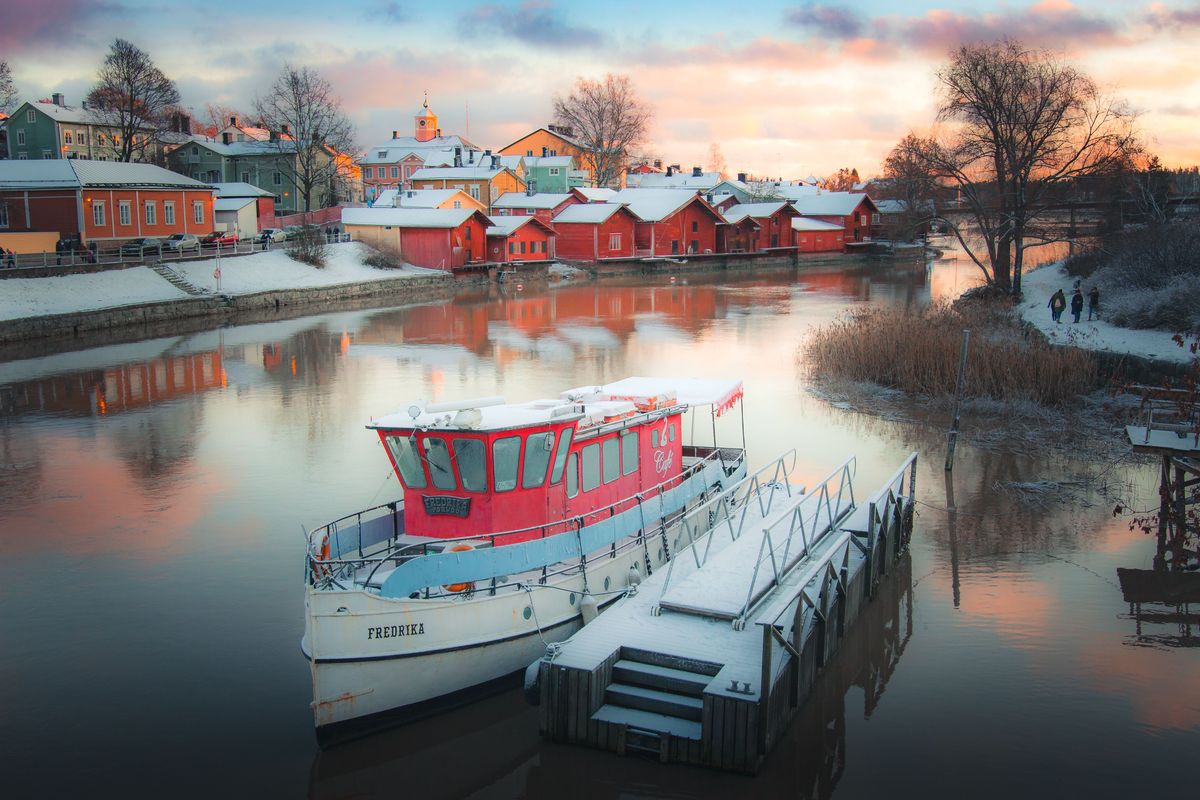Tradiční barevné dřevěné domy ve městě Porvoo se zrcadlí na hladině řeky, s&nbsp;kotvící lodí Fredrika v&nbsp;popředí.