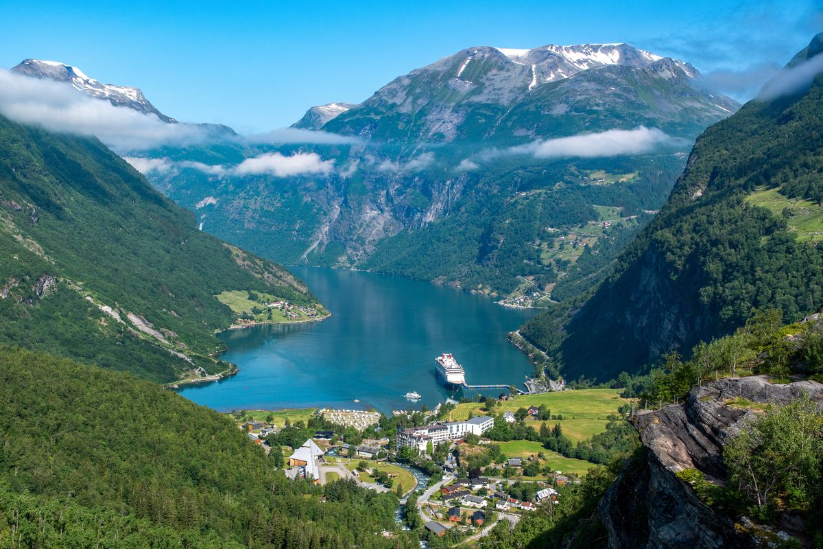 Geirangerfjord v Norsku s majestátními horami a malým přístavem, kde kotví výletní loď obklopená zelenými svahy.