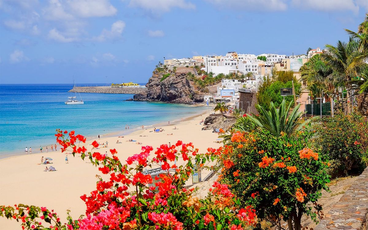 Písečná pláž v Morro Jable na ostrově Fuerteventura s tyrkysovým Atlantským oceánem a malebnou vesnicí na pobřeží.