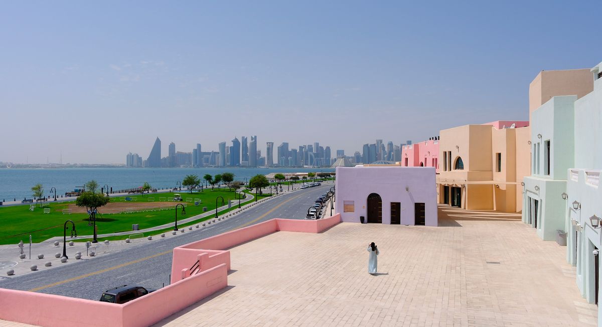 Pohled na moderní panorama města Doha v&nbsp;Kataru s&nbsp;tradičními pastelově zbarvenými domy v&nbsp;popředí.