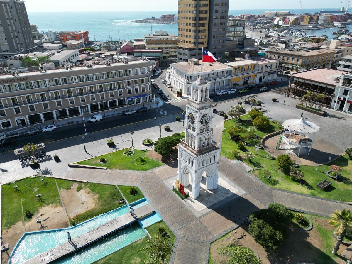 Pohled na věžové hodiny na náměstí Prat ve městě Iquique s&nbsp;pozadím městské zástavby a&nbsp;Tichého oceánu.