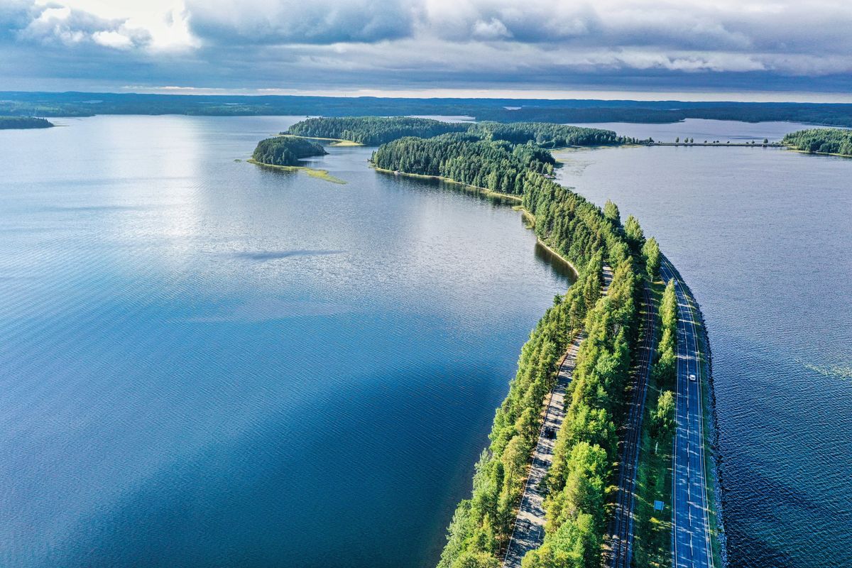 Silnice vinoucí se přes jezero Reijolanjaiz v&nbsp;nádherné finské krajině, obklopená hustými lesy a&nbsp;klidnou vodní plochou.