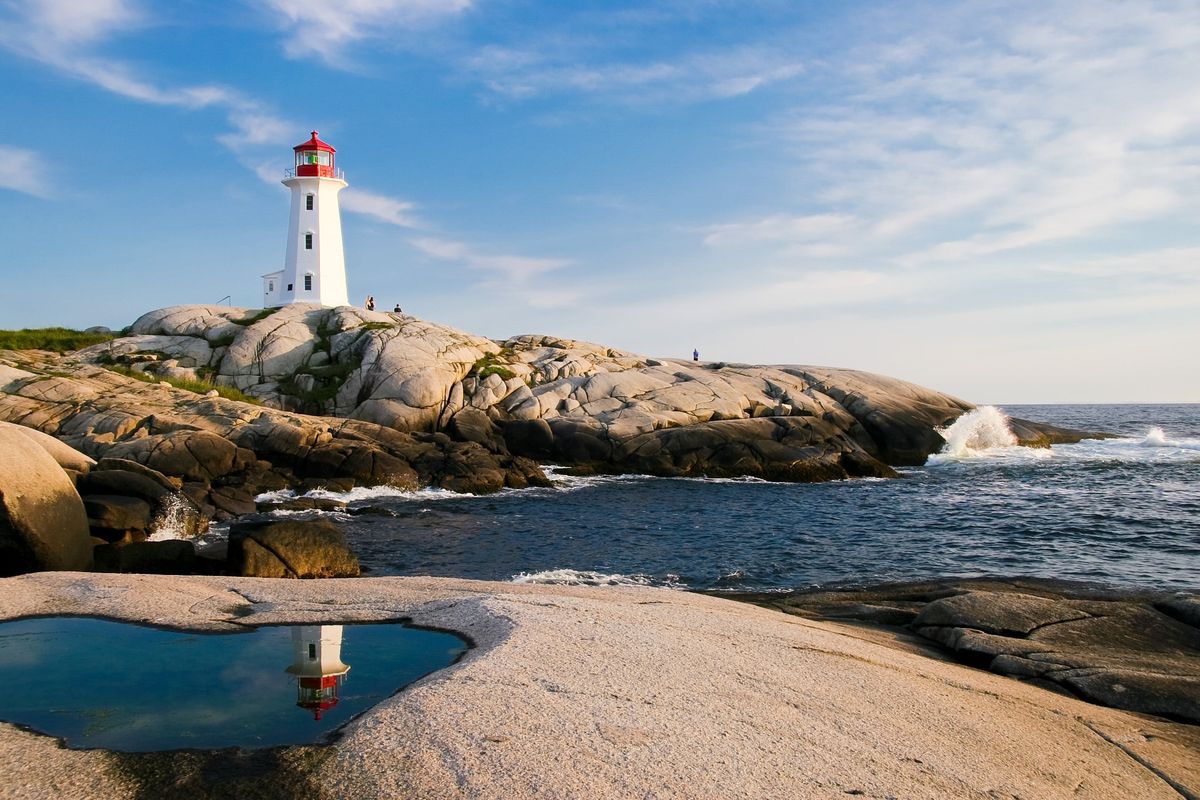 Maják Peggy's Cove v&nbsp;Novém Skotsku je zasazen na skalnatém pobřeží s&nbsp;vlnami tříštícími se o&nbsp;útesy pod modrou oblohou.