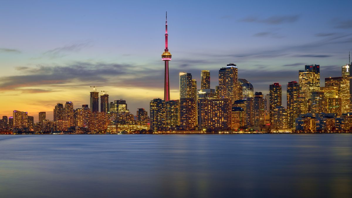 Panorama Toronta s&nbsp;dominantní věží CN Tower při západu slunce, odrážející se na vodní hladině.