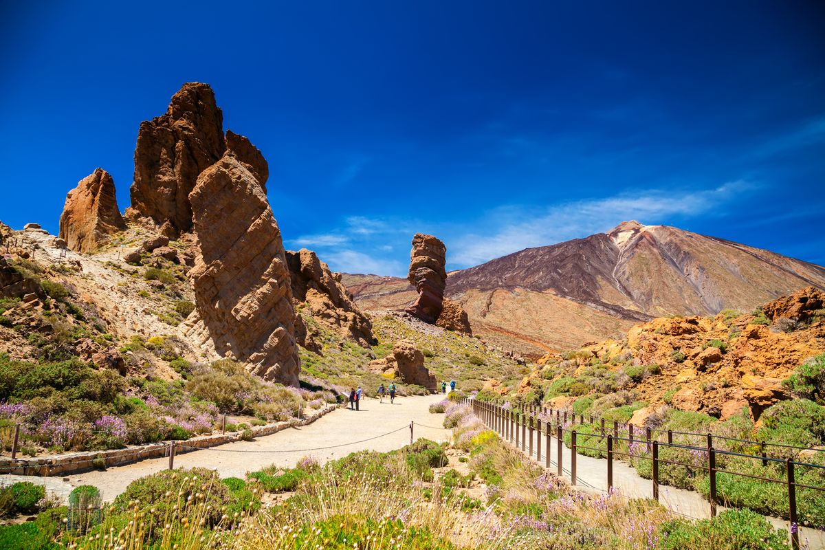 Pohled na majestátní Pico del Teide, nejvyšší horu Španělska, obklopenou sopečnými skalními útvary a kvetoucí přírodou na Tenerife.