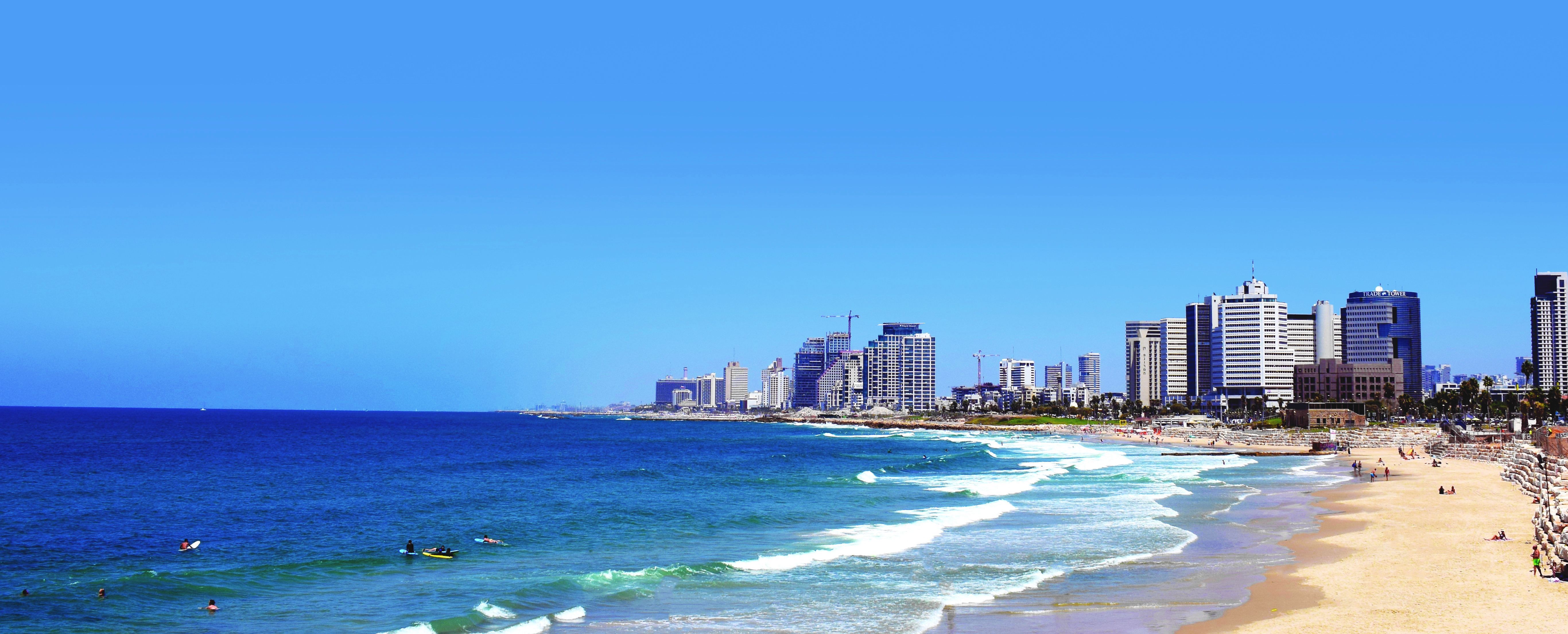 Panoráma pobřeží města Tel Aviv se sluncem zalitou pláží a&nbsp;moderními mrakodrapy podél Středozemního moře.