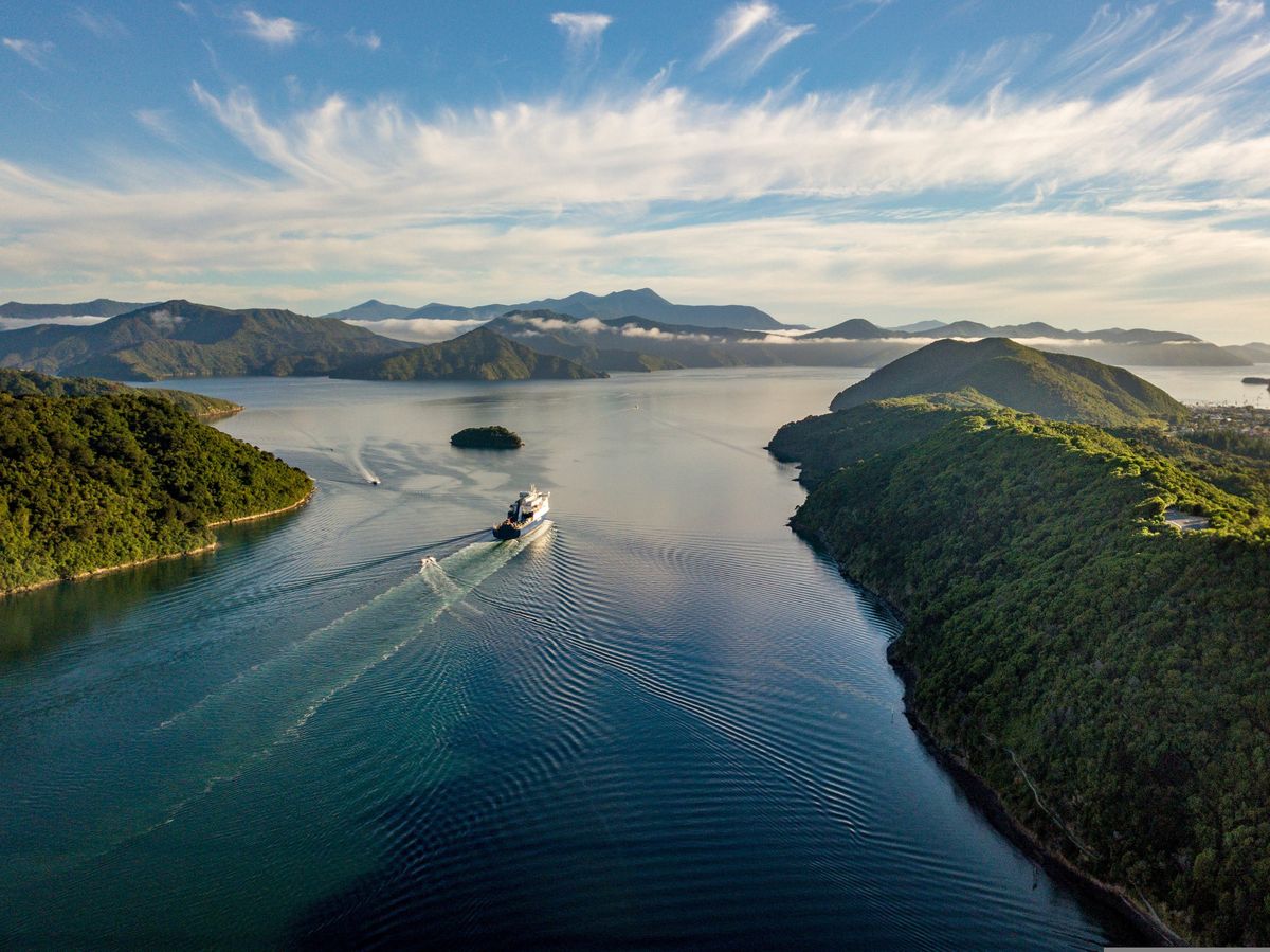 Trajekt cestuje klidnými vodami mezi zelenými kopci v&nbsp;oblasti Marlborough Sounds na Novém Zélandu.