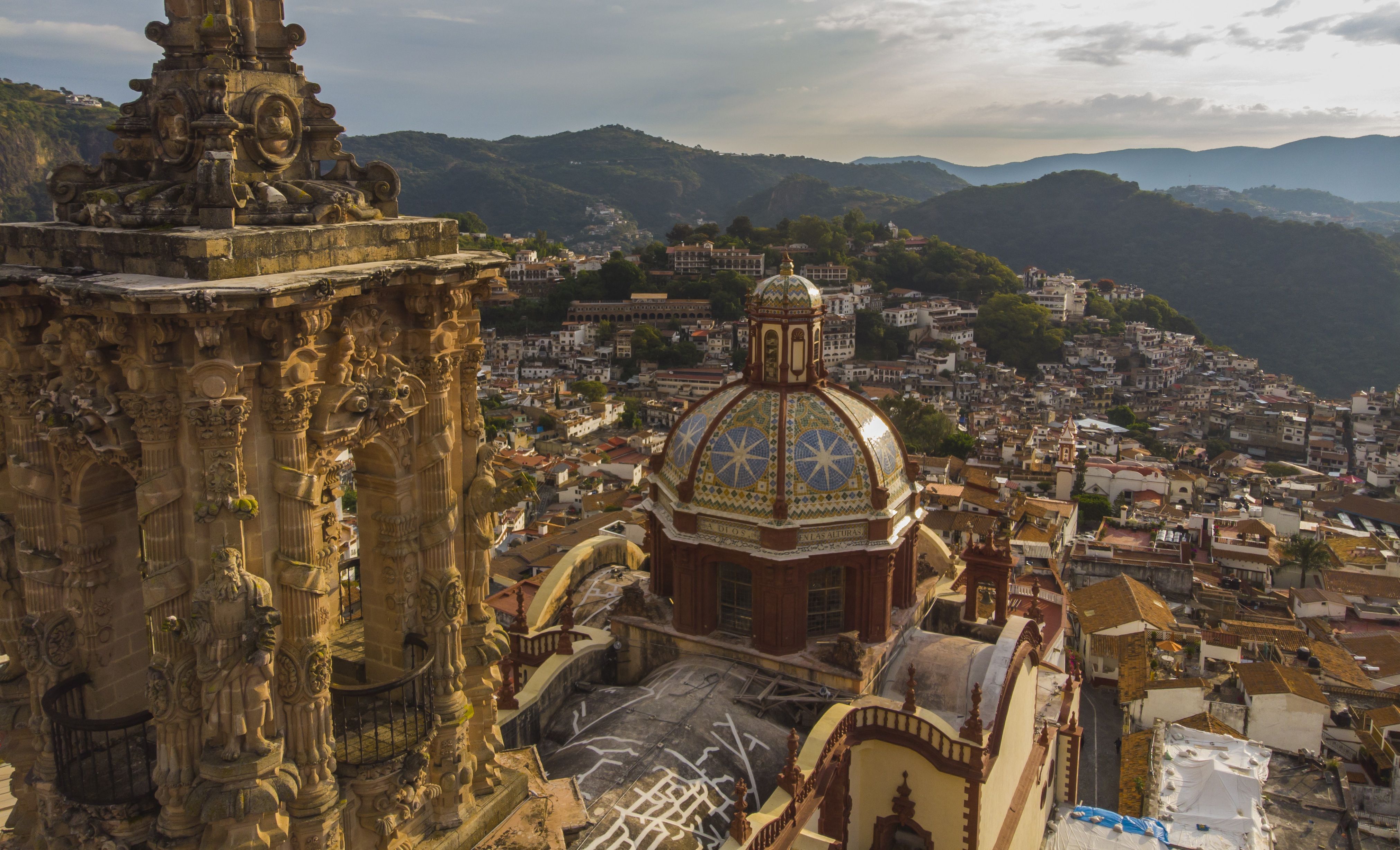 Barokní chrám Santa Prisca se tyčí nad kopcovitým městem Taxco obklopeným zelenými horami.