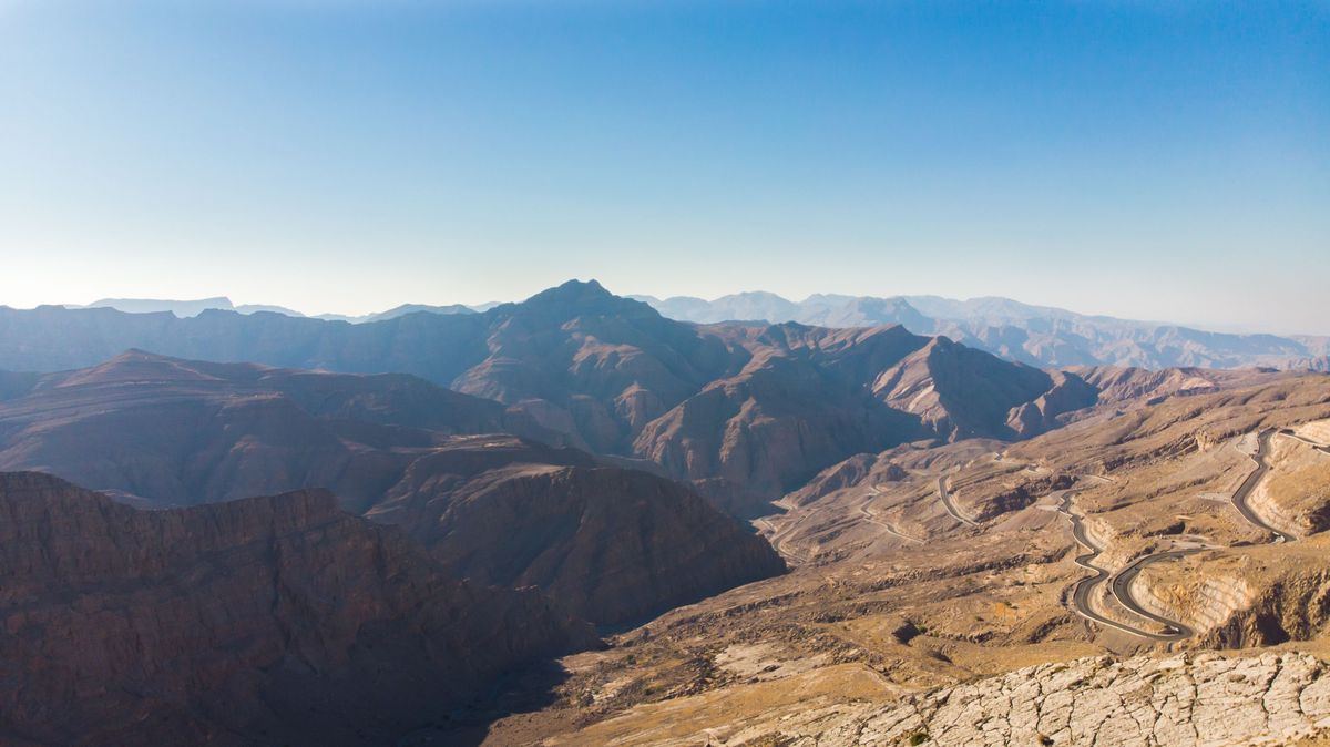 Panoramatický pohled na hornaté údolí v emirátu Ras al-Khaimah se silnicí vinoucí se skrz suchý terén.