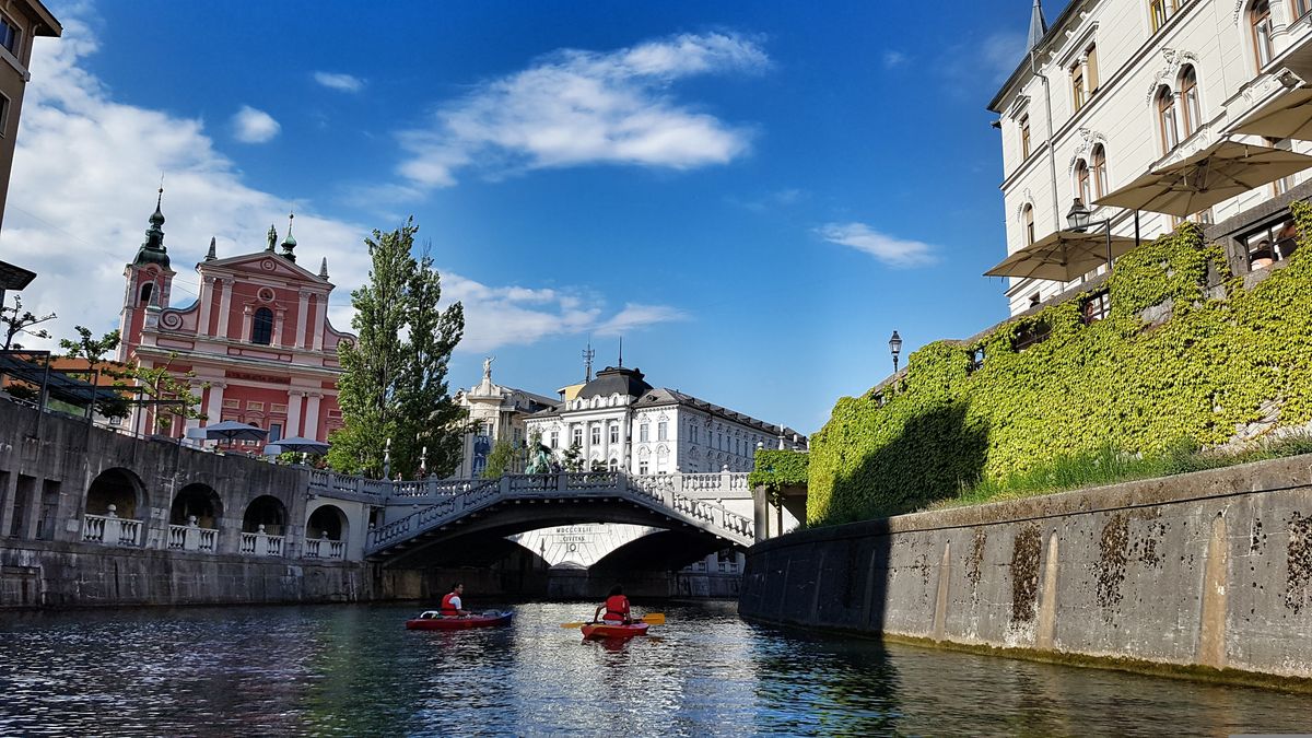 Pohled na Tromostovje v Lublani se slavnou růžovou františkánskou církví a lidmi na kajaku na řece Lublanici.
