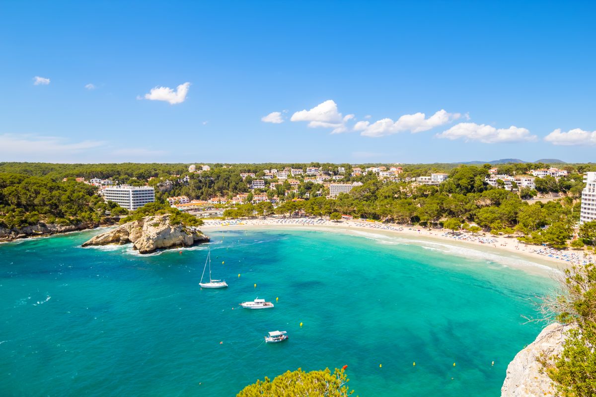 Pohled na pláž Cala Galdana s tyrkysovým mořem, obklopenou piniovými lesy a hotely na ostrově Menorca.