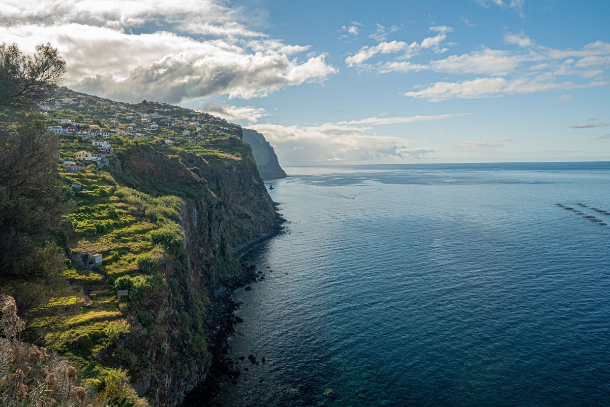 Strmá pobřežní útes poblíž vesničky s&nbsp;terasovitými poli ústí do Atlantského oceánu na ostrově Madeira, Portugal.