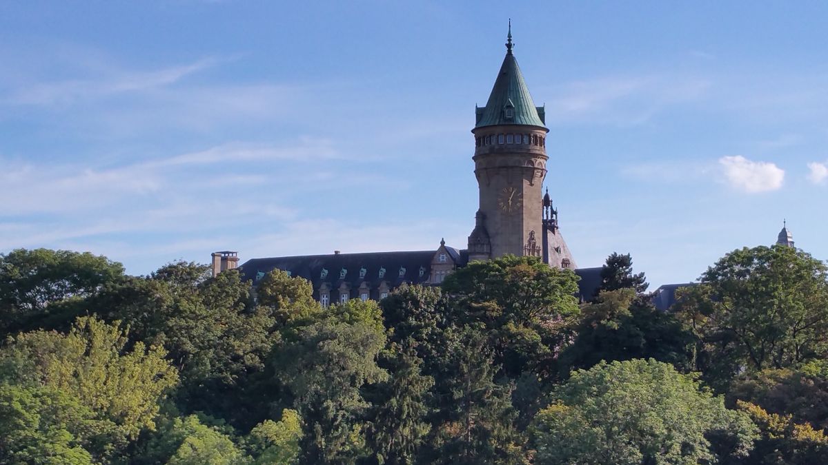 Historická věž budovy Spaarbank na pozadí modré oblohy je obklopena bujnou zelení v&nbsp;Lucemburku.