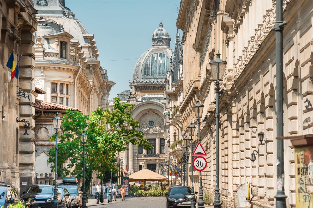 Historická ulice v&nbsp;centru Bukurešti s&nbsp;dominantní budovou CEC Palace v&nbsp;pozadí, obklopená ozdobnými budovami a&nbsp;lemovaná stromy.