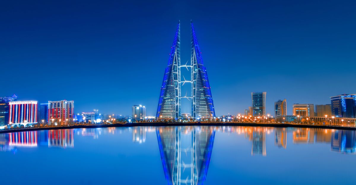 Pohled na osvětlené mrakodrapy Bahrain World Trade Center v&nbsp;Manamě odrážející se ve vodní hladině.
