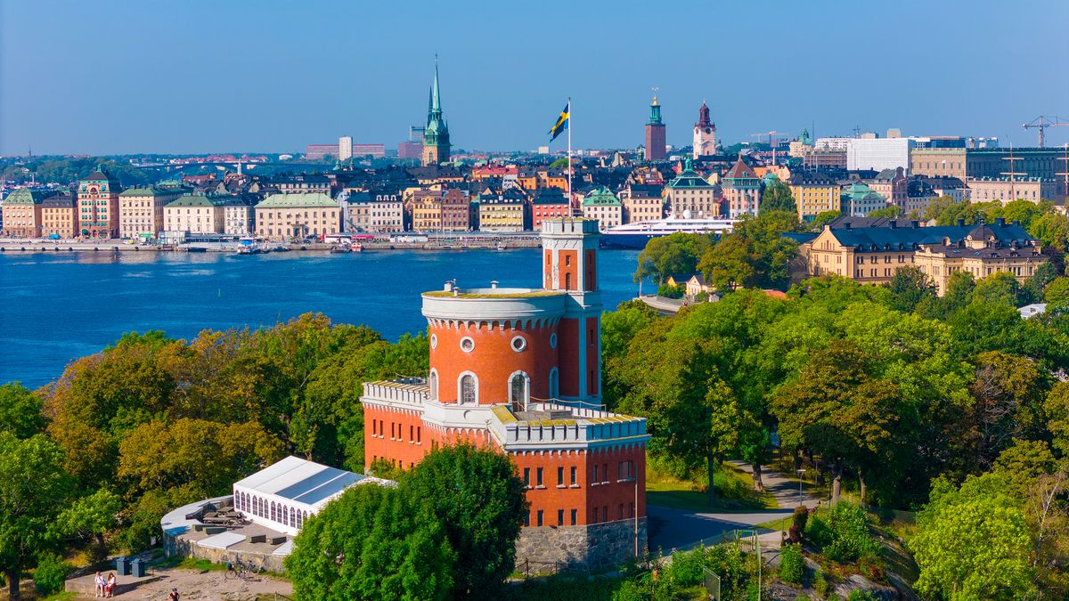 Budova Kastellet v Stockholm v popředí, obklopená zelení a s výhledem na městské panorama za vodou.