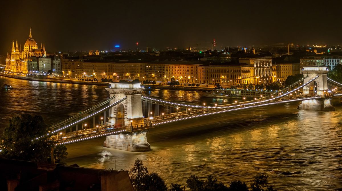 Noční pohled na osvětlený Řetězový most v Budapešti přes řeku Dunaj s budovou parlamentu v pozadí.