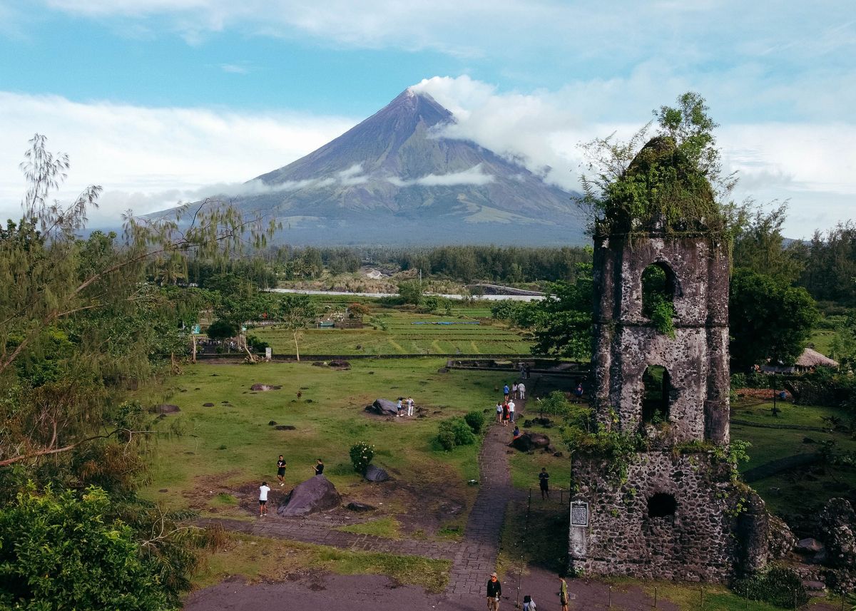 Vulkán Mayon se vypíná majestátně nad ruinami kostela Cagsawa obklopeného zelenými poli na Filipínách.
