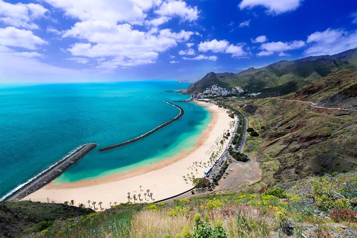 Pláž Las Teresitas na severovýchodě Tenerife se rozkládá podél křišťálově modrého moře s dlouhým pásmem zlatavého písku a je lemována palmami.