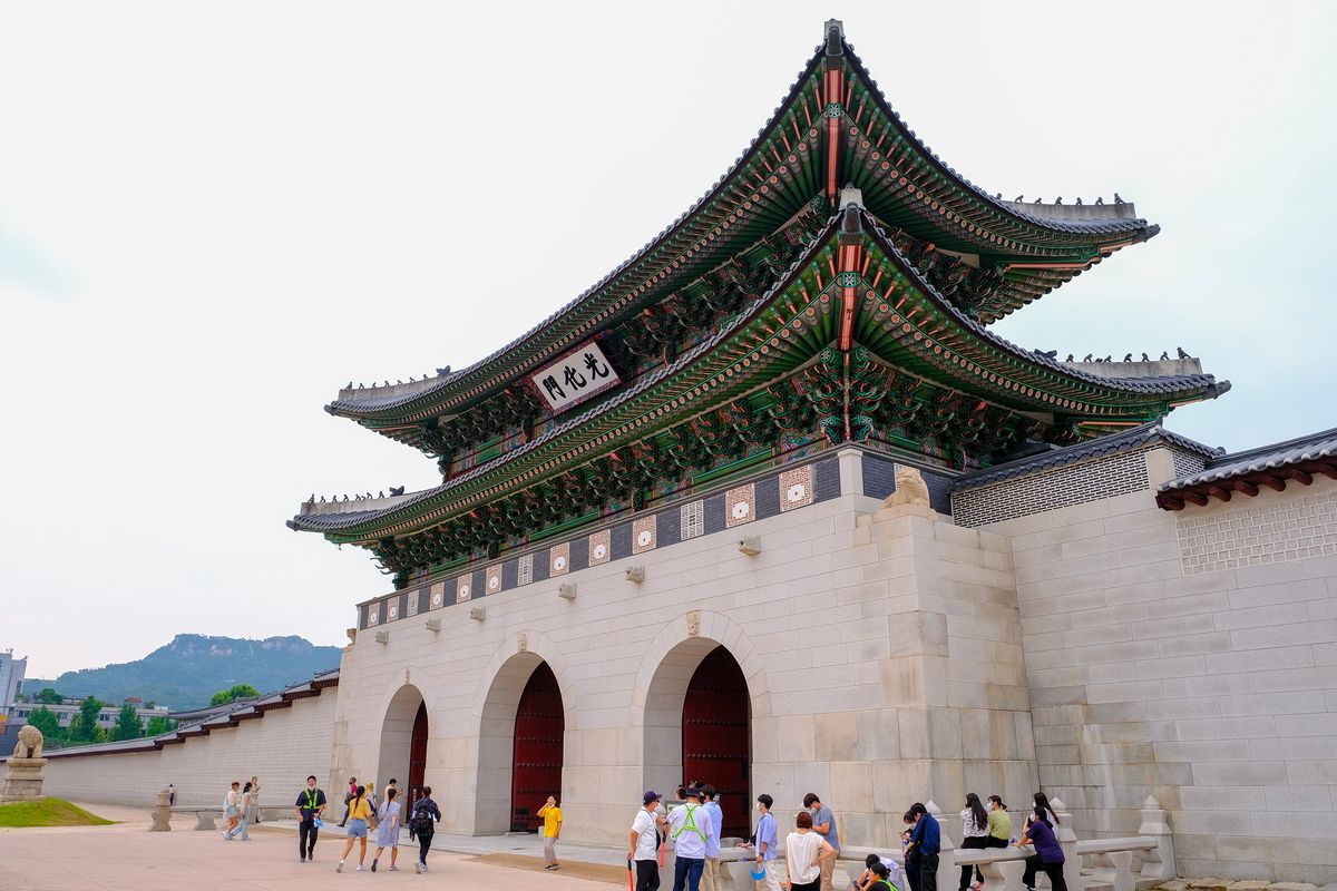 Hlavní brána Gwanghwamun je součástí královského paláce Gyeongbokgung a&nbsp;je obklopena návštěvníky. Nachází se v&nbsp;centru Soulu s&nbsp;horou v&nbsp;pozadí.