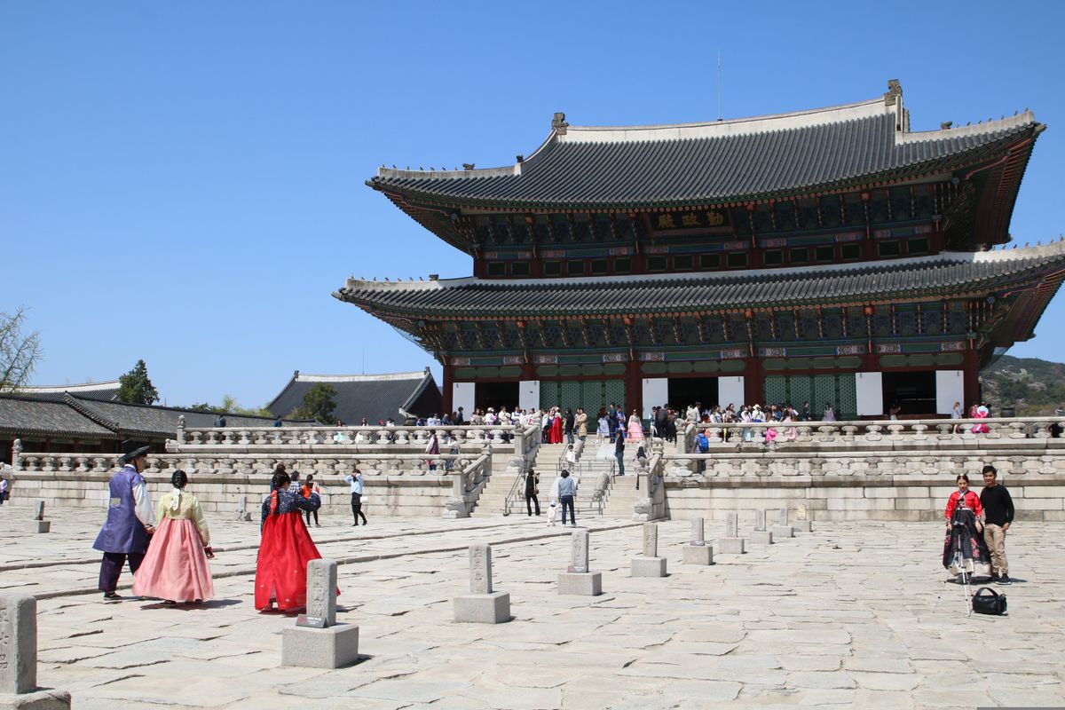 Tradiční korejská architektura paláce Gyeongbokgung v&nbsp;Soulu se skupinou návštěvníků v&nbsp;hanbocích na nádvoří.