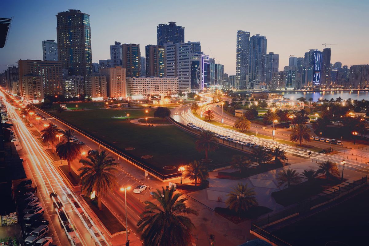 Rušná večerní scéna města Ajman ve Spojených arabských emirátech s osvětlenými mrakodrapy a živými ulicemi.