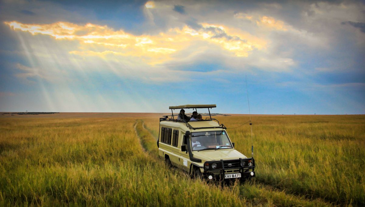 Safari terénní vůz projíždí přes savanu v&nbsp;Masai Mara za slunečného počasí.