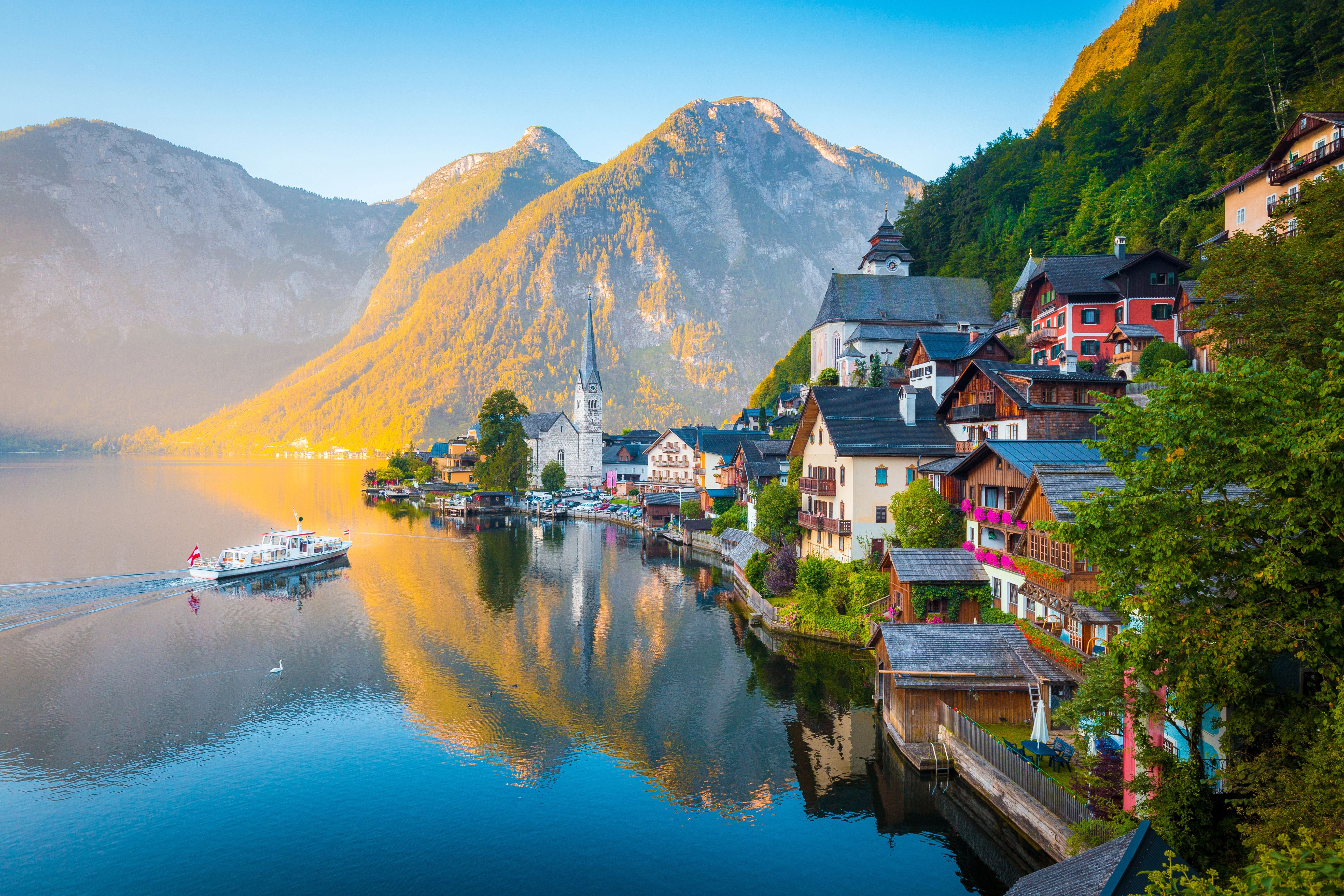 Malebná obec Hallstatt leží na břehu Hallstattského jezera, obklopená impozantními Alpami, s typickými alpskými domy a kostelem u vody.