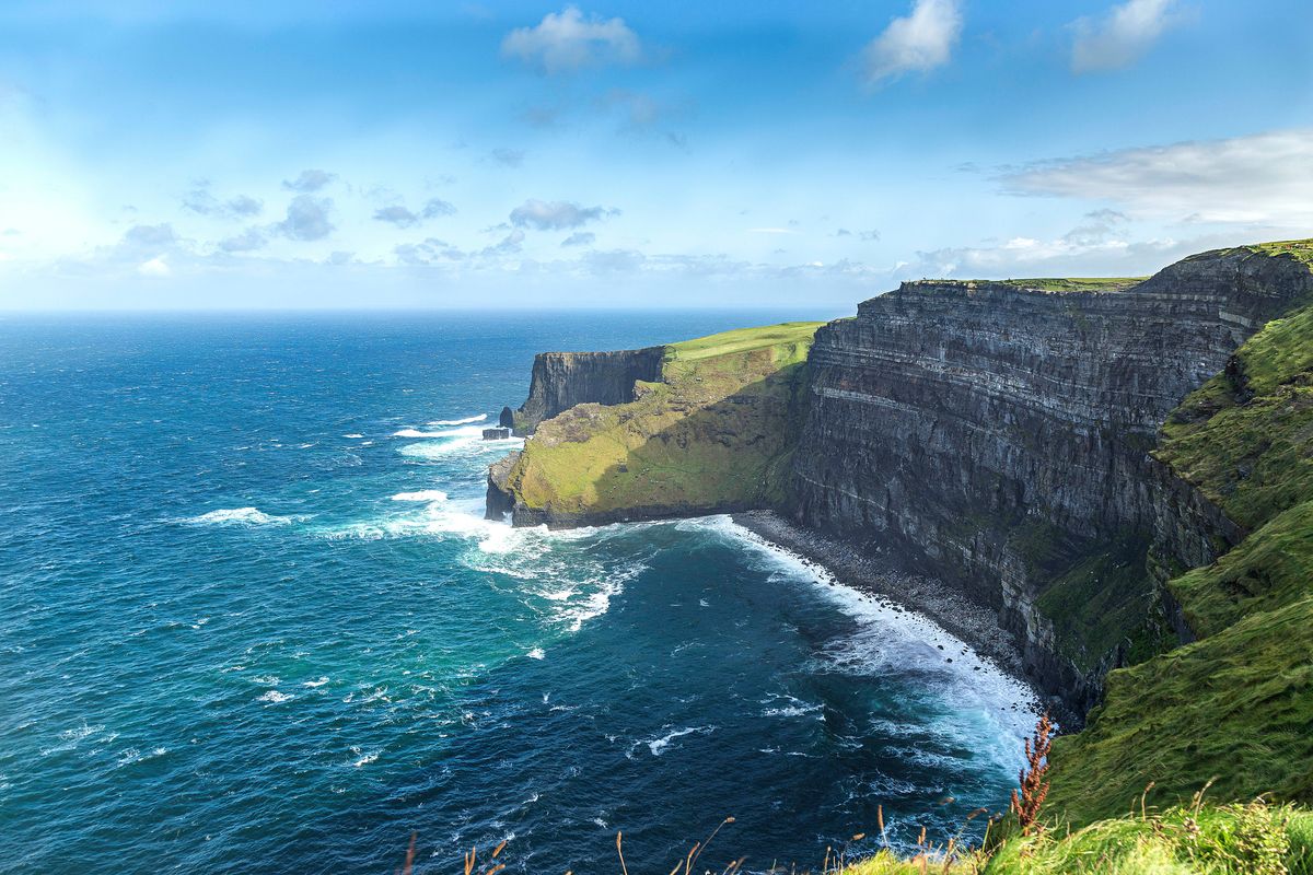 Strmé Cliffs of Moher v&nbsp;Irsku se tyčí nad modrým Atlantským oceánem, přičemž jejich vápencová vrstva se dramaticky zvedá z&nbsp;mořské hladiny.