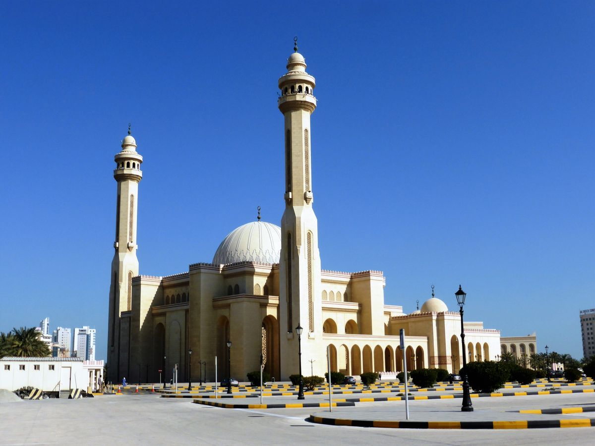 Velká mešita Al-Fatih v Manámě s dvěma minarety a kopulí na pozadí modré oblohy.
