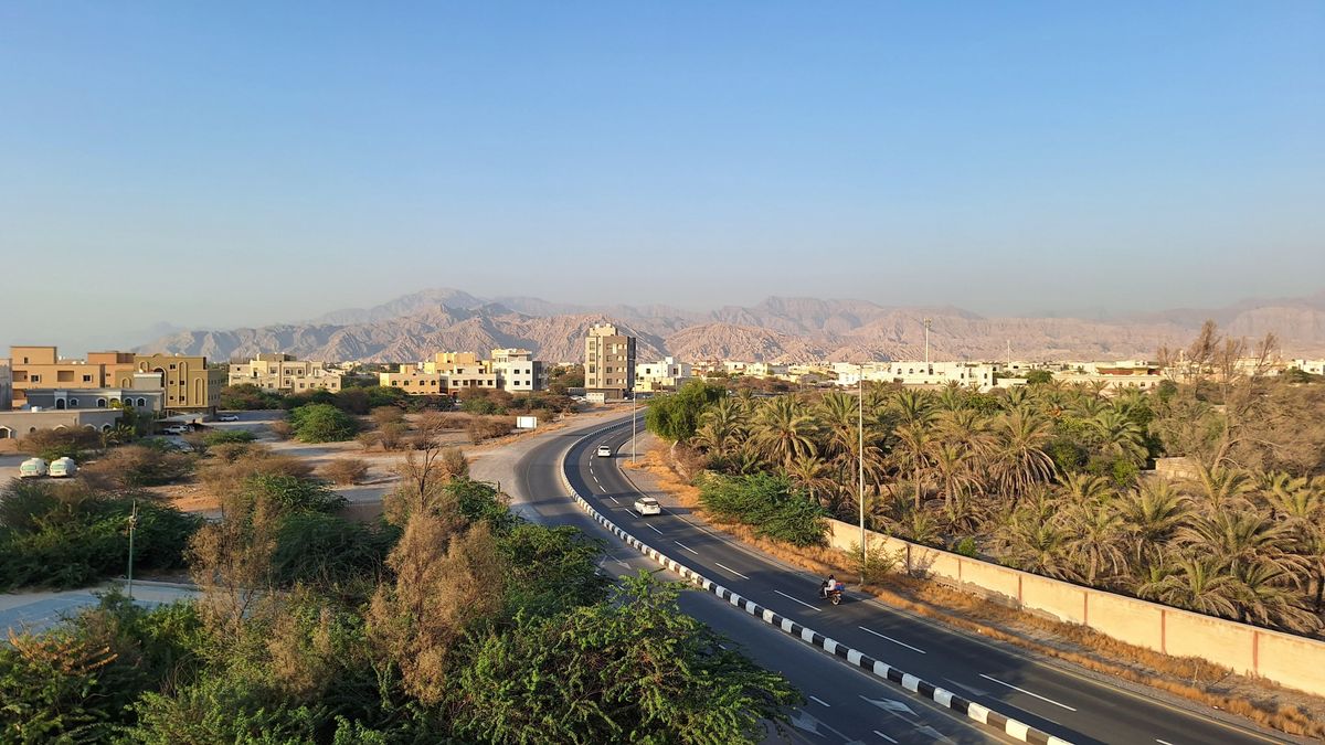 Ras al-Khaimah, město ve Spojených arabských emirátech, obklopené horami a zelení s klidnou silnicí vedoucí skrz čtvrť s moderními domy.