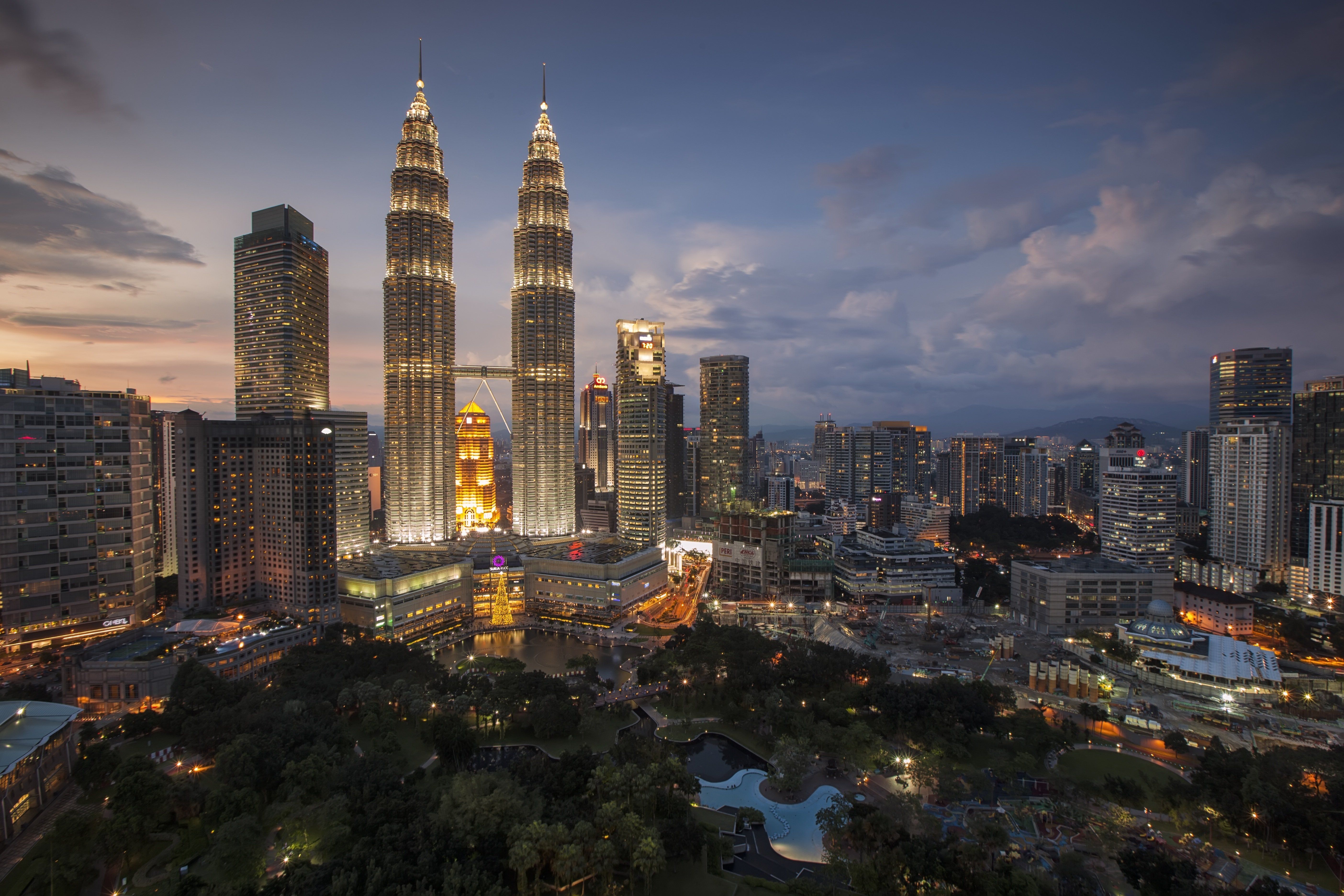 Panorama Kuala Lumpuru při soumraku s osvícenými Petronas Twin Towers v popředí a okolními moderními mrakodrapy.