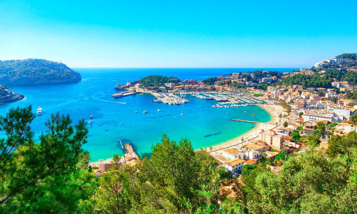 Přístavní městečko Port de Sóller na Mallorce s přístavem plným lodí a malebným okolím v údolí mezi horami Serra de Tramuntana.