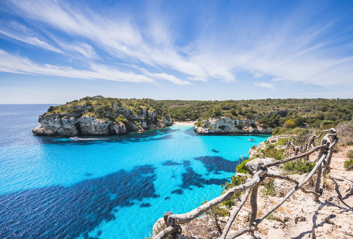 Pohled na tyrkysově modré moře obklopené vysokými skalami a zelení na ostrově Menorca ve Španělsku.