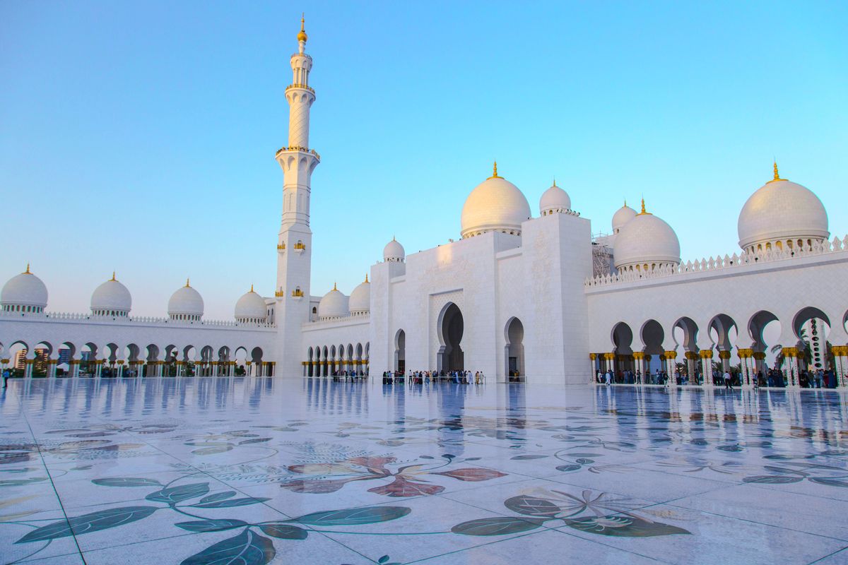 Velká mešita šejka Zayeda v Abú Dhabí se svými bílými mramorovými kopulemi a minaretky odrážejícími se na rozlehlé podlaze dvora.