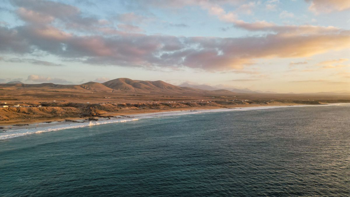 Fuerteventura na Kanárských ostrovech při západu slunce nabízí pohled na širokou pláž lemovanou jemnými kopci, které se táhnou do dáli pod dramatickou oblohou.