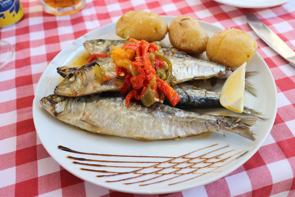 Talíř s&nbsp;grilovanými sardinkami, bramborami a&nbsp;paprikami podávaný v&nbsp;regionu Portugalsko, ozdobený citronem na kostkovaném ubrusu.