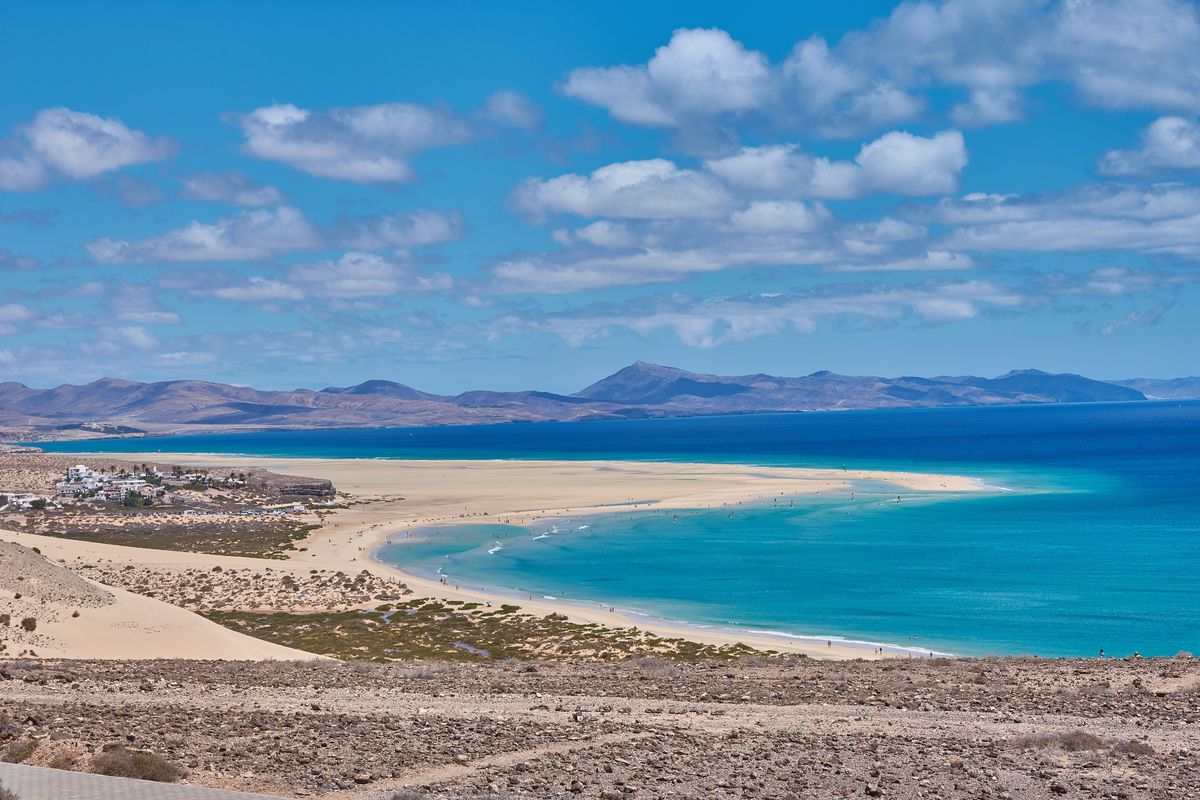 Pohled na malebnou pláž Cofete s dlouhým písčitým pobřežím na ostrově Fuerteventura, obklopenou horami a tyrkysovým mořem.