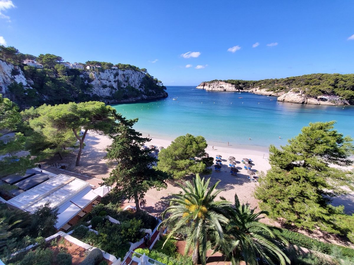 Krásná písčitá pláž obklopená borovicemi a tyrkysovým mořem na ostrově Menorca, ideální pro rekreaci a relaxaci.