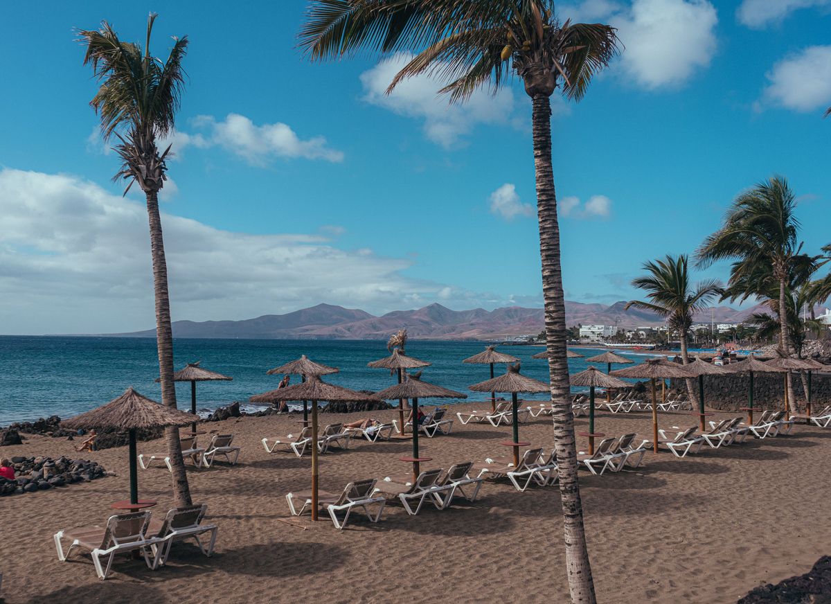 Pláž na ostrově Lanzarote s palmovými stromy a lehátky, obklopena Atlantským oceánem.