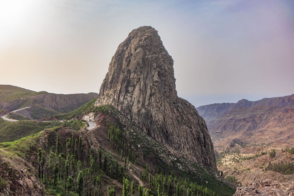 Skalní útvar Roque de Agando na ostrově La Gomera, obklopený bujnou vegetací a strmými svahy.