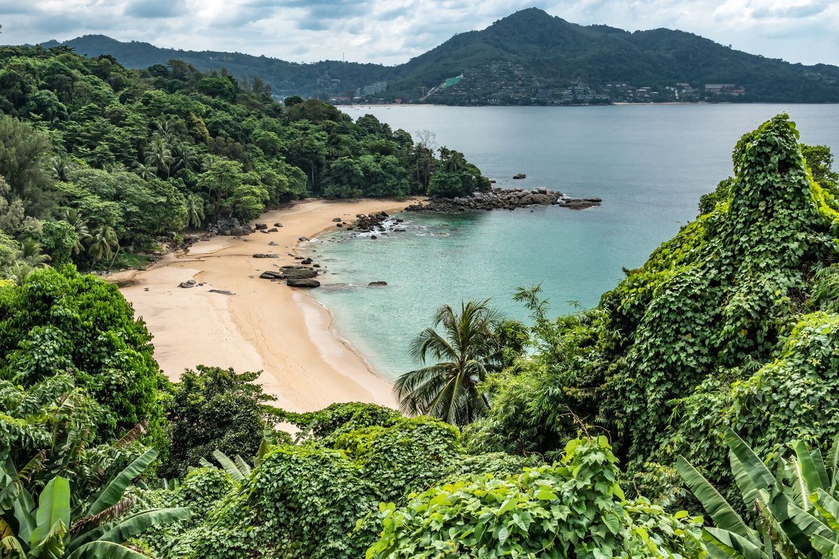 Tropická pláž obklopená hustou džunglí a skalními útvary na thajském ostrově Phuket.