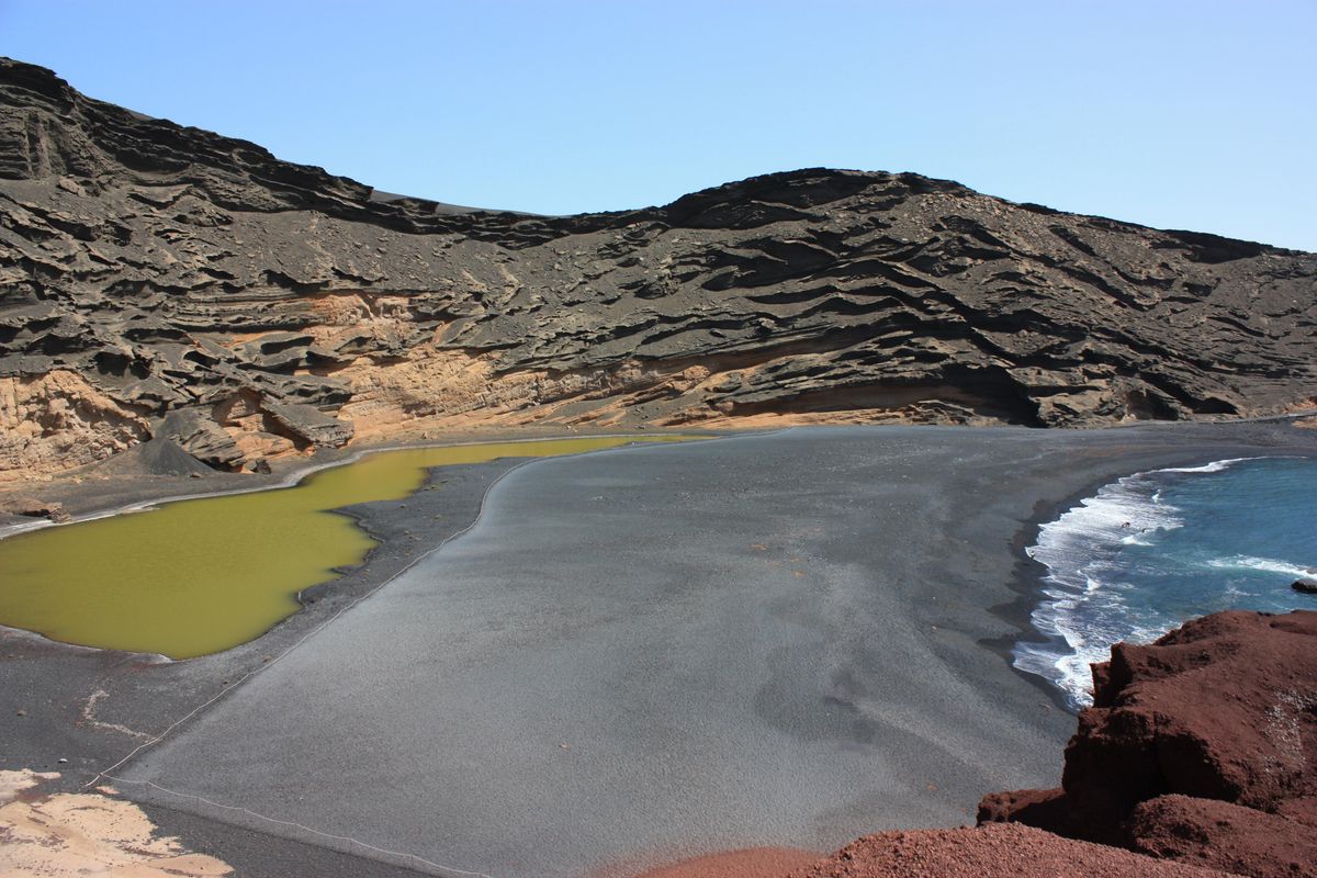 Zelené jezero Charco de los Clicos na černé písčité pláži obklopené vulkanickými útesy na Lanzarote.