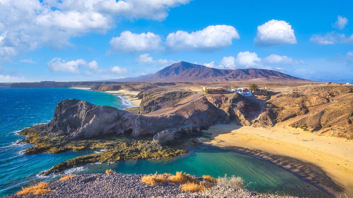 Scenérie s pohledem na malebnou pláž Papagayo na ostrově Lanzarote s dramatickou vulkanickou krajinou v pozadí.