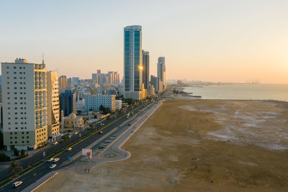 Pohled na panorama města Ajman ve Spojených arabských emirátech s výškovými budovami podél pobřežní cesty při západu slunce.