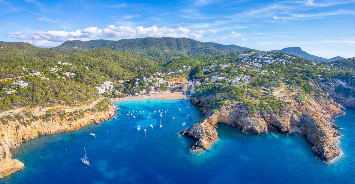 Vzdušný pohled na malebnou zátoku Cala Vadella s tyrkysovým mořem a okolními zelenými kopci na ostrově Ibiza ve Španělsku.